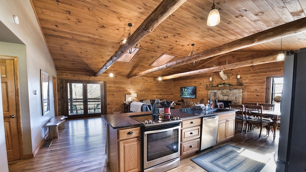 A spacious kitchen with wooden cabinets, a large island, and a stone fireplace. - Hocking Hills log cabin with guest house on 12 private acres with pond (Logan)