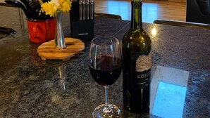 A kitchen counter with a wine glass, a bottle of wine, a vase with flowers, and a knife block. - Hocking Hills log cabin with guest house on 12 private acres with pond (Logan)