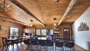 A spacious kitchen with wooden beams, a central island with bar stools, and a dining area with a leather couch. - Hocking Hills log cabin with guest house on 12 private acres with pond (Logan)