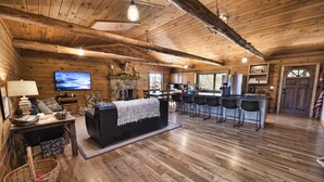 A rustic cabin interior with a living area, kitchen, and bar seating. - Hocking Hills log cabin with guest house on 12 private acres with pond (Logan)
