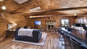 A log cabin interior with a living room, fireplace, kitchen, and a large window. - Hocking Hills log cabin with guest house on 12 private acres with pond (Logan)