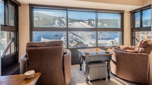 A room with large windows offering a view of a ski slope. There are two brown armchairs and a small wooden table. - The best view in Center Village.  Perfect for Concerts and Skier watching!!! (Copper Mountain)