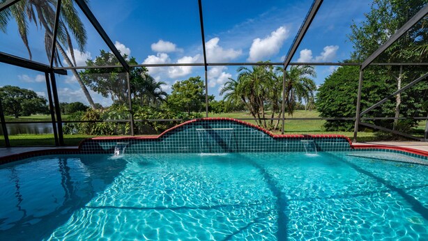 Une piscine d’un bleu éclatant, bordée de carreaux, entourée d’une clôture en métal et de palmiers.