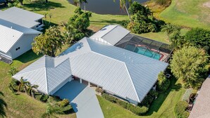 Une maison moderne dotée d’une grande piscine, entourée d’une végétation luxuriante et d’un étang.
