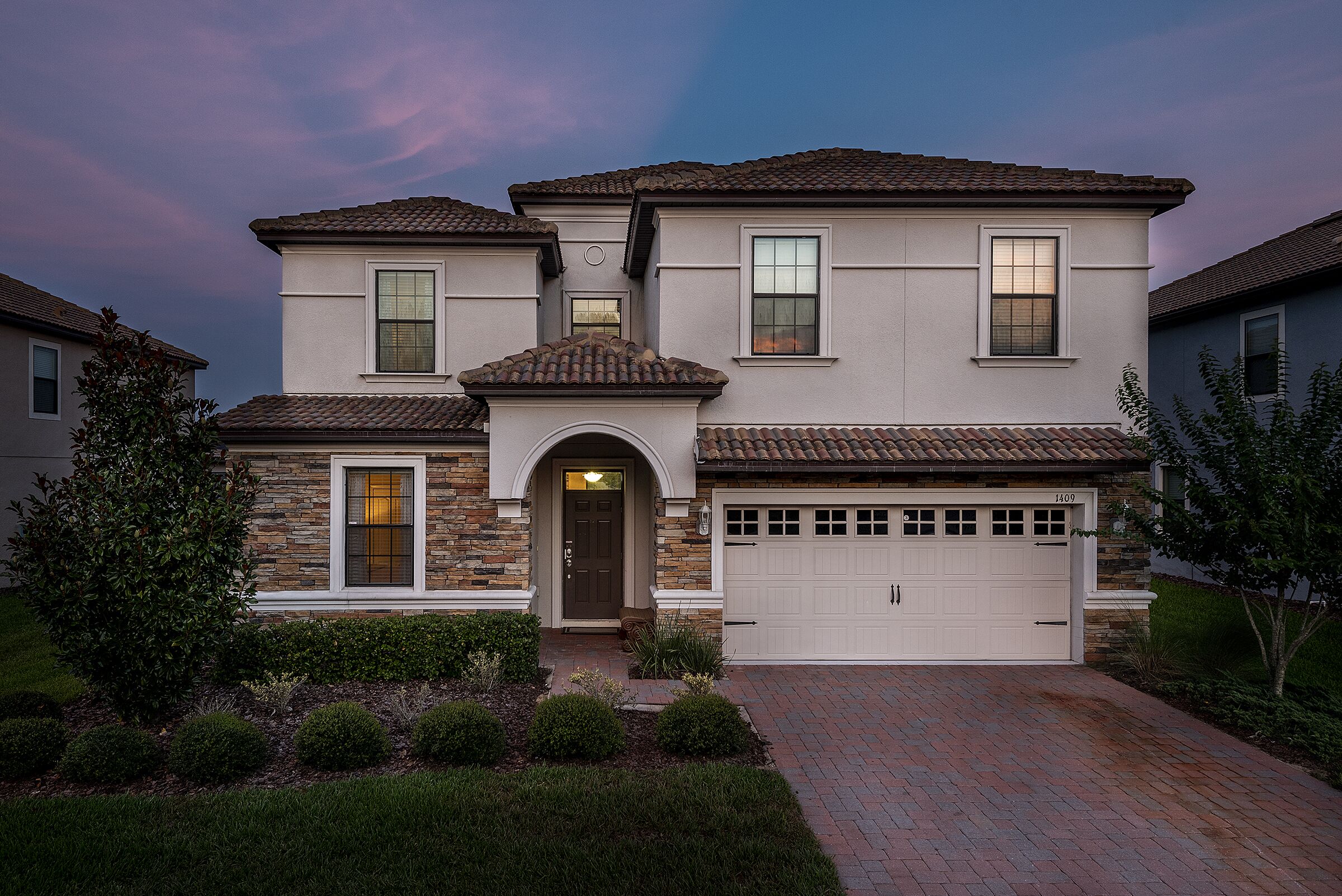 A two-story house with a garage, stone facade, and a well-maintained front yard.