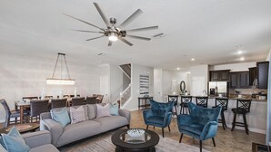 A spacious living room with a gray sectional sofa, two blue armchairs, a round coffee table, and a ceiling fan.