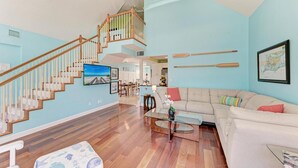 A spacious living room with a wooden staircase, a large sofa, and a dining area.
