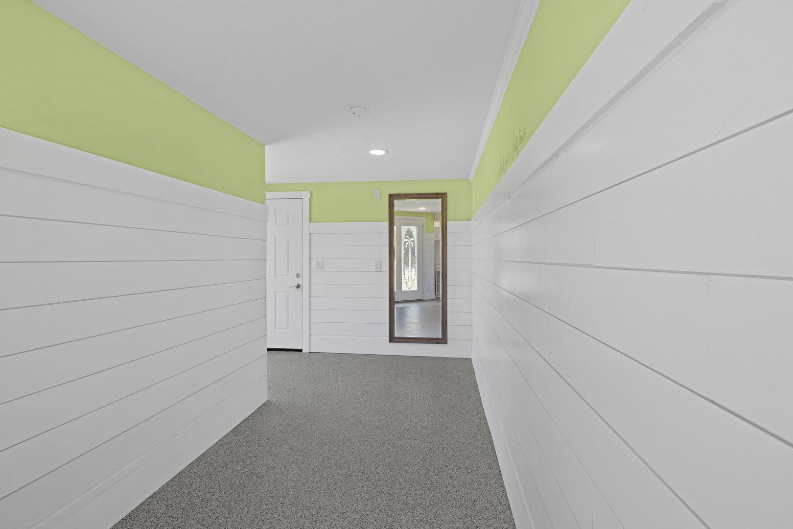 A narrow hallway with white paneling on the walls and a grey carpet.