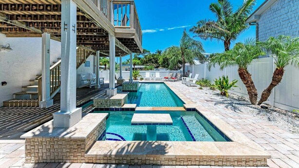 A swimming pool with a stone border, a covered seating area, and a staircase leading to an upper level.