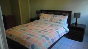 A bed with a colorful polka dot bedspread, two bedside tables with lamps, and a wooden headboard.