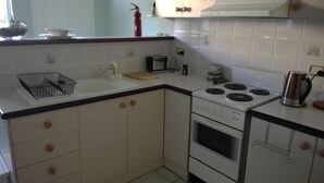 A compact kitchen with white cabinets, a stove, a sink, and a small countertop.
