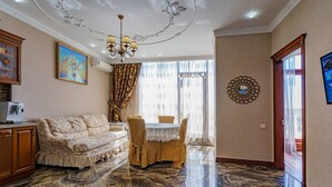 Ein Zimmer mit Marmorboden, einer Couch, einem Esstisch mit Stühlen, einer Chandelüstere und einem Gemälde an der Wand.