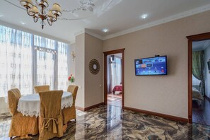 Une chambre d’hôtel dotée d’un coin repas agrémenté d’un lustre, d’un téléviseur fixé au mur et offrant une vue sur l’extérieur par une porte.