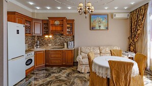 Eine Küche mit Holzausstattung, einem weißen Kühlschrank und einer Arbeitswand aus Stein. Ein Essbereich mit Tisch und Stühlen sowie eine Couch sind ebenfalls vorhanden.