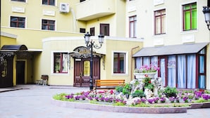 Ein Gebäude mit gelber Fassade, einer Holzbank und einem Blumenbeet im Innenhof.