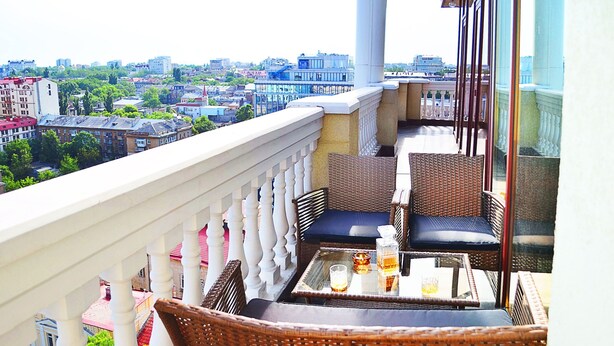 Ein Balkon mit Korbmöbeln, einem Glastisch und Blick auf die Stadt.