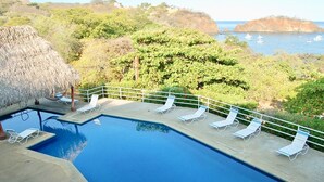 A swimming pool with lounge chairs and a thatched roof structure.