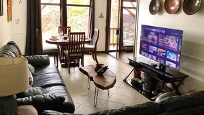 A living room with a sofa, a coffee table, a TV, and a dining area with chairs and a table.