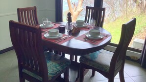 A dining table set for four with chairs, a view of the outdoors, and a painting on the wall.