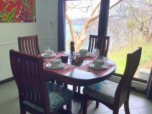 A dining table set for four with chairs, a view of the outdoors, and a painting on the wall.