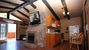 A spacious living area with a stone fireplace, wooden cabinets, and a television mounted above it. - Gatlinburg Cabin, Free Tickets, Secluded Mtn Views, Hot Tub, Heart Tub, Internet (Gatlinburg)
