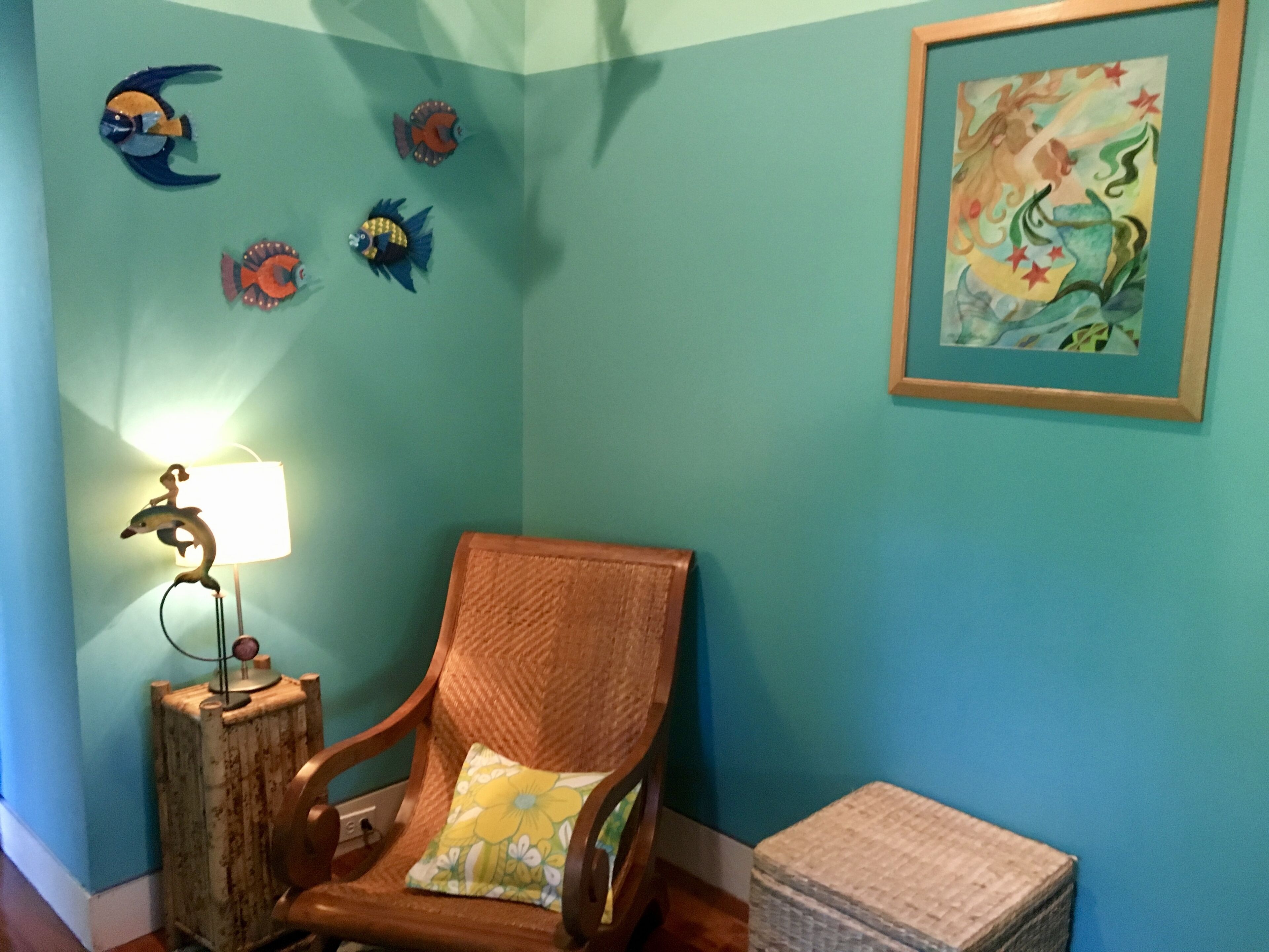 Una stanza dalle pareti color acquamarina, con una sedia di legno, una lampada e decorazioni a tema pesci sulle pareti.