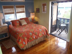 Un dormitorio con cama, mesitas de noche, lámpara, ventana con persianas y puerta que da a un espacio exterior con una silla.