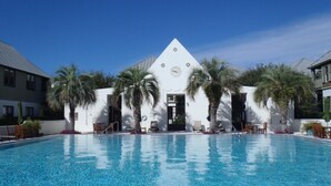 Ein Swimmingpool mit einem weißen Gebäude im Hintergrund, Palmen und blauem Himmel.