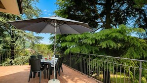 An outdoor dining area with a table and chairs, a large umbrella, and a metal railing. - Villa Alberti Apt Emma 900m from Garda lake w/ shared Garden, Salò, Italy (Salò)