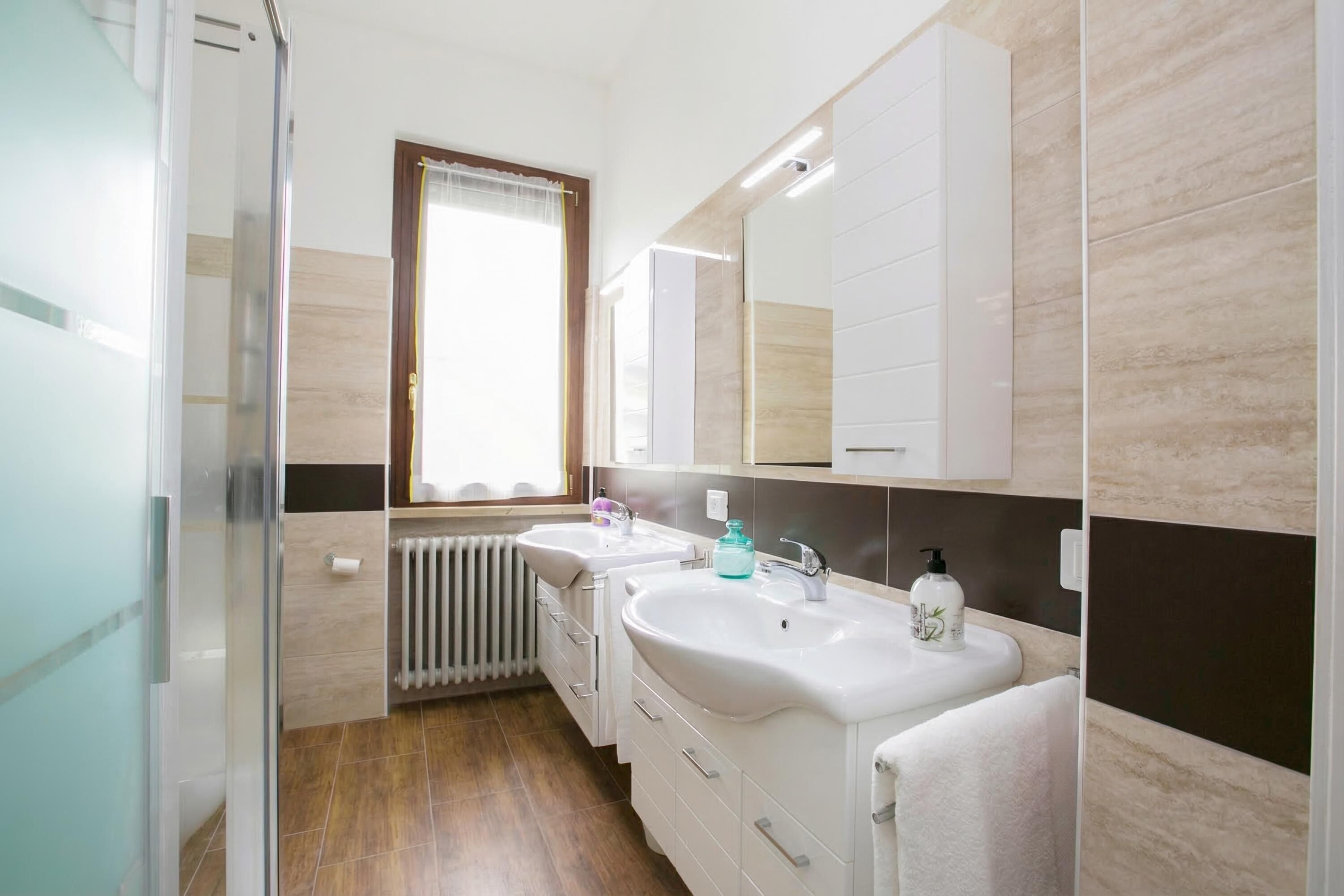 A modern bathroom with two sinks, a mirror, and a window.