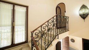 A staircase with ornate black metal railings, a wooden handrail, and a wall-mounted light fixture. - Villa Alberti Apt Emma 900m from Garda lake w/ shared Garden, Salò, Italy (Salò)