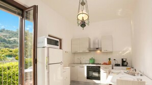 A compact kitchen with a built-in microwave, oven, and sink, a dining table with chairs, and a balcony with a view of greenery. - Villa Alberti Apt Emma 900m from Garda lake w/ shared Garden, Salò, Italy (Salò)