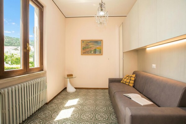 A living room with a sofa, a radiator, a glass table, a painting, and a window with a view.