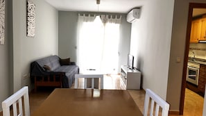 Un espacio habitable compacto con sofá, mesa de comedor, televisor y kitchenette.