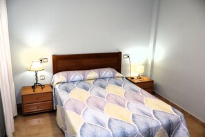 Un dormitorio con una cama de madera, dos mesitas de noche con lámparas y una colcha estampada.