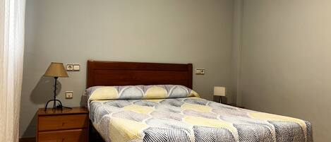 A bedroom with a wooden bed, a nightstand, a lamp, and a wall socket.