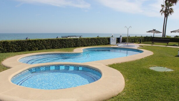 A swimming pool with a curved design, surrounded by a well-maintained lawn and a hedge. - 171 Medina Molins (Denia)