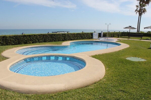 A swimming pool with a curved design, surrounded by a well-maintained lawn and a hedge.