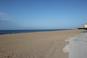 A wide sandy beach with a clear blue sky and calm sea.