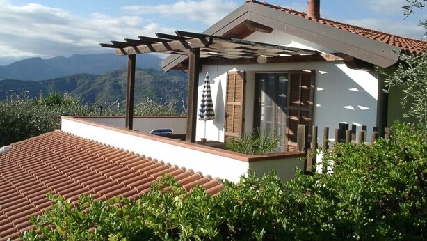 Una casa con pérgola en el techo, una chimenea y vistas a las montañas.