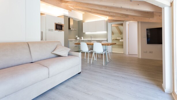 Una sala moderna con un sofá, un comedor con sillas y una cocina con armarios y microondas.