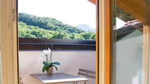 Un balcón abierto con una mesa y sillas, una planta en maceta y vistas a una zona boscosa.
