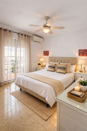 A bedroom with a bed, ceiling fan, bedside lamps, a nightstand, a window with curtains, and a view of the outdoors.