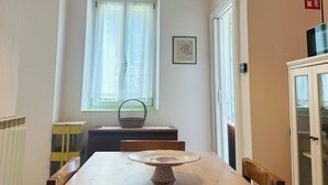 Ein Essbereich mit einem Holztisch, Stühlen, einer Hängelampe, einem fenster mit Vorhängen, einem Heizkörper und einem Schrank.