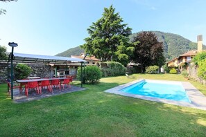 A backyard with a swimming pool, a barbecue area, and a large tree.