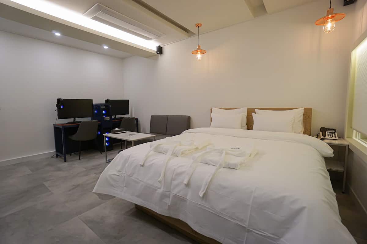 A hotel room with a bed, a desk with a computer, a chair, and a telephone.