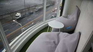Una habitación moderna con un ventanal curvo, una pequeña mesa blanca y un sofá gris.