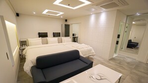 Una habitación de hotel moderna con una cama grande, un sofá negro, un escritorio blanco y un espejo amplio.
