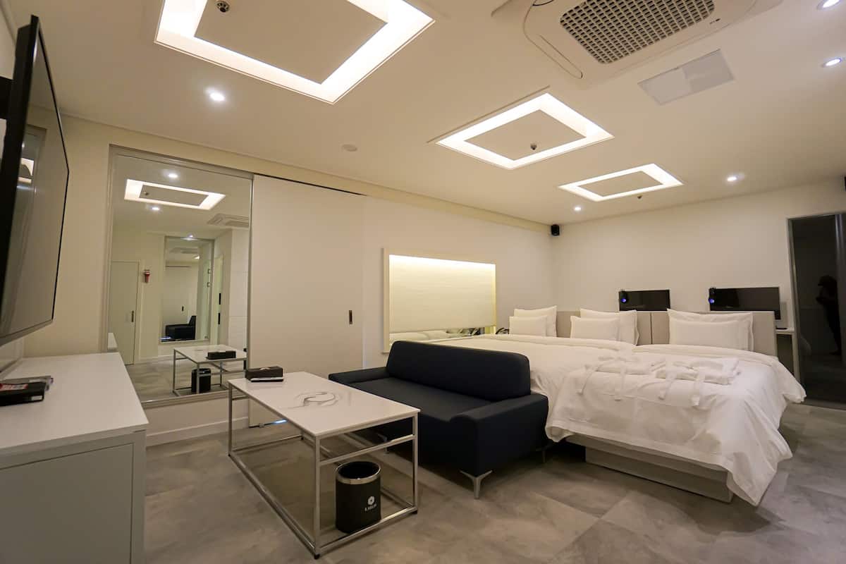 A modern hotel room with a large bed, a desk, a sofa, and a mirror.