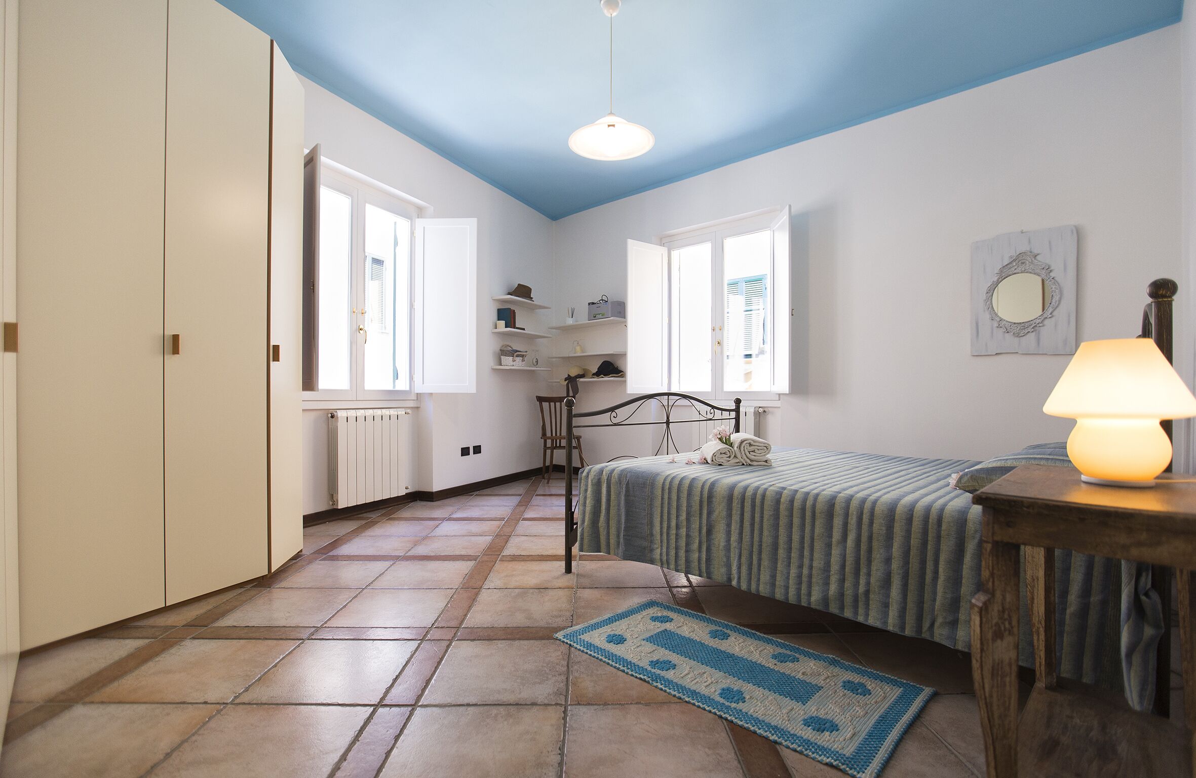 A bedroom with a bed, a nightstand, a lamp, a dresser, and a window.
